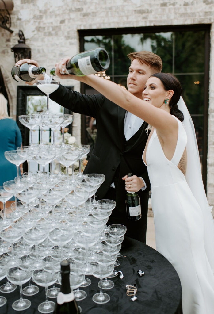 Fort Worth Texas luxury wedding venue reception featuring bride and groom in designer custom wedding gown and tuxedo pouring champagne into a champagne tower
