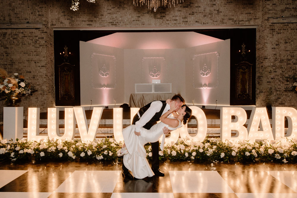 Fort Worth Texas luxury wedding reception with bride and groom kissing in front of light up marquee letters and fresh flower installations