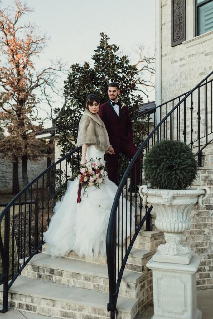 Bride and groom wearing luxury designer wedding dress and black designer suit post on a grand staircase at a secret garden wedding venue near Fort Worth